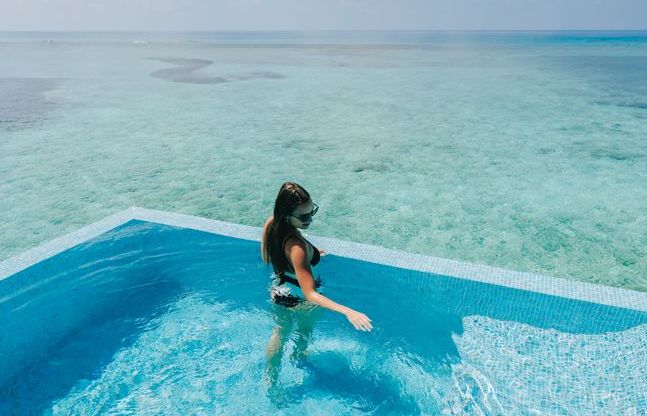 VARU by Atmosphere, North Malé Atoll: a guest wading in a water villa pool over the lagoon