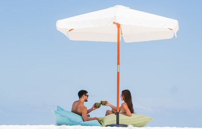 VARU by Atmosphere, North Malé Atoll: a couple with coconuts under an umbrella on a sandbank