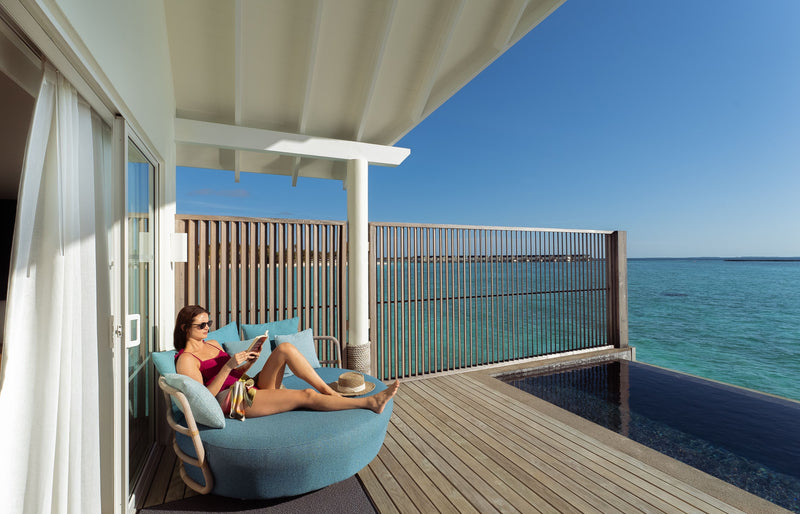 RAAYA by Atmosphere, Raa Atoll: a guest reading on the deck of a water villa with pool