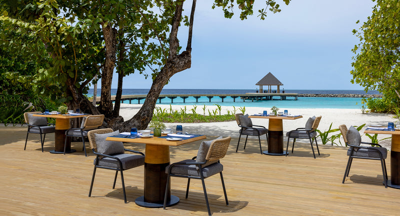 Ocean Terrace tables on the sand at Avani+ Fares Maldives, with a jetty gazebo behind.