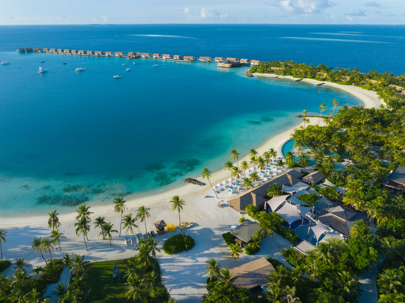 Waldorf Astoria Maldives Ithaafushi, South Malé Atoll: a curving white-sand beach and pool, with a line of overwater villas across the lagoon