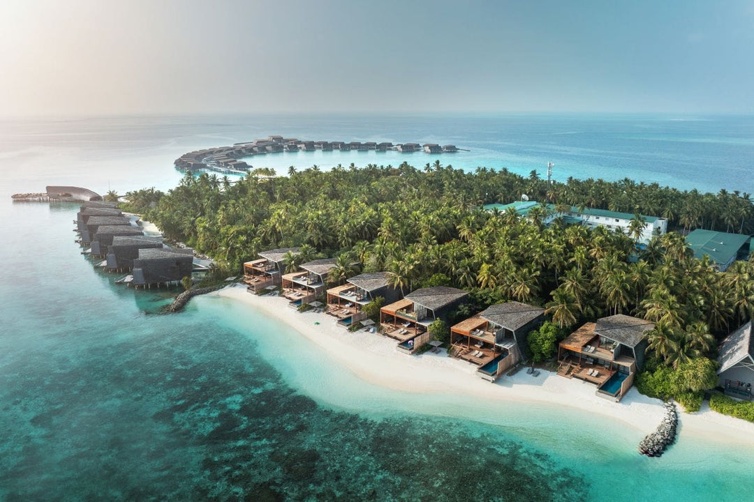 The St. Regis Maldives Vommuli, Dhaalu Atoll — Aerial of the island, beach villas along the sand and overwater villas curving into the lagoon