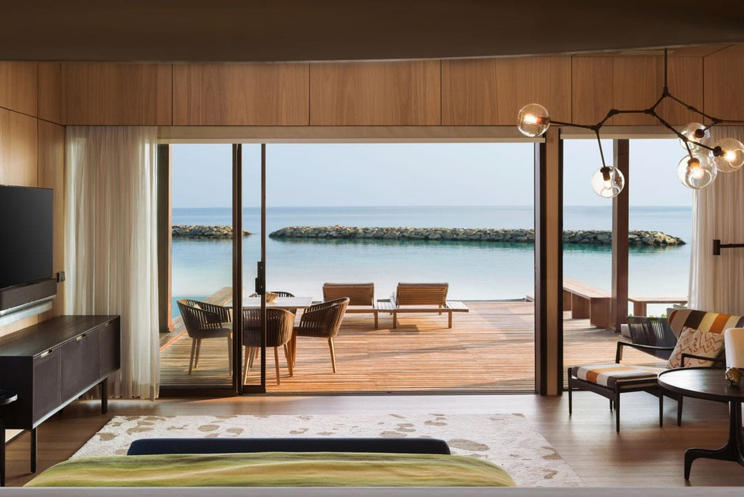 The St. Regis Maldives Vommuli, Dhaalu Atoll — Bedroom with folding glass doors onto a deck with loungers and a breakwater beyond