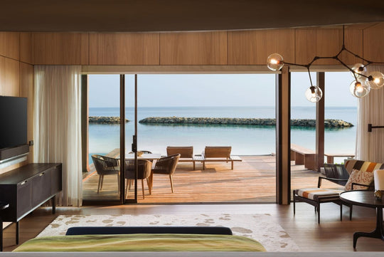 The St. Regis Maldives Vommuli, Dhaalu Atoll — Bedroom with folding glass doors onto a deck with loungers and a breakwater beyond