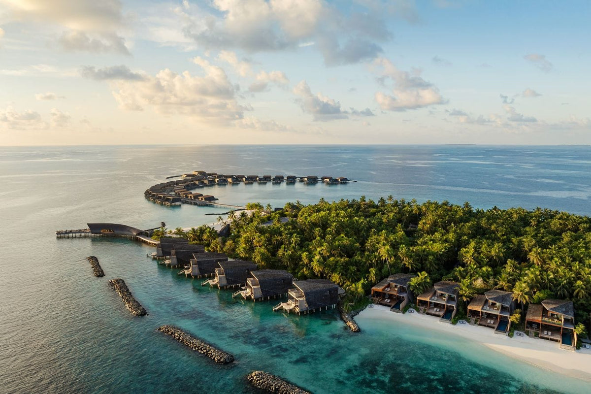 The St. Regis Maldives Vommuli Resort at first light, overwater villas along the shore of a densely wooded island