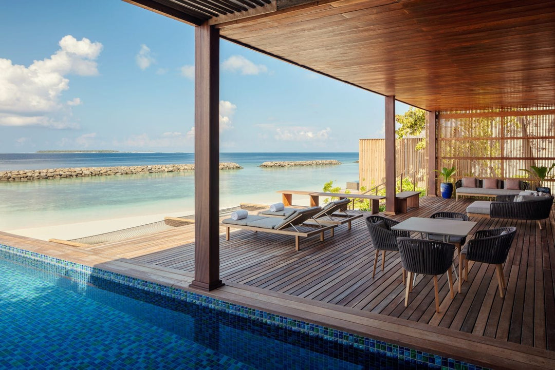 The St. Regis Maldives Vommuli, Dhaalu Atoll — Covered terrace with a dining table and lounge seating beside a pool, the sea beyond
