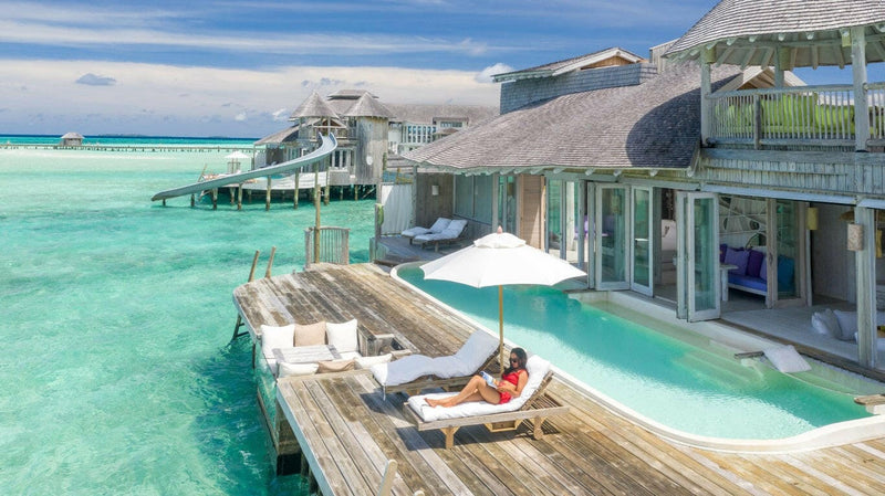 A water villa at Soneva Jani seen from the lagoon, a white parasol and plunge pool on the timber deck.