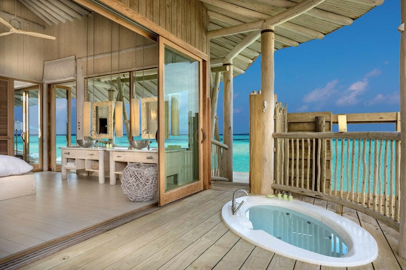 A villa deck at Soneva Jani, an oval bath sunk in the boards outside a pale timber bathroom.