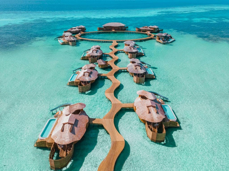 Overwater retreats at Soneva Jani from the air, round thatched roofs strung along a curving walkway.