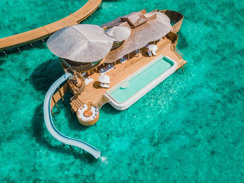 A water villa at Soneva Jani from directly above, a long deck pool and a slide looping into the reef.