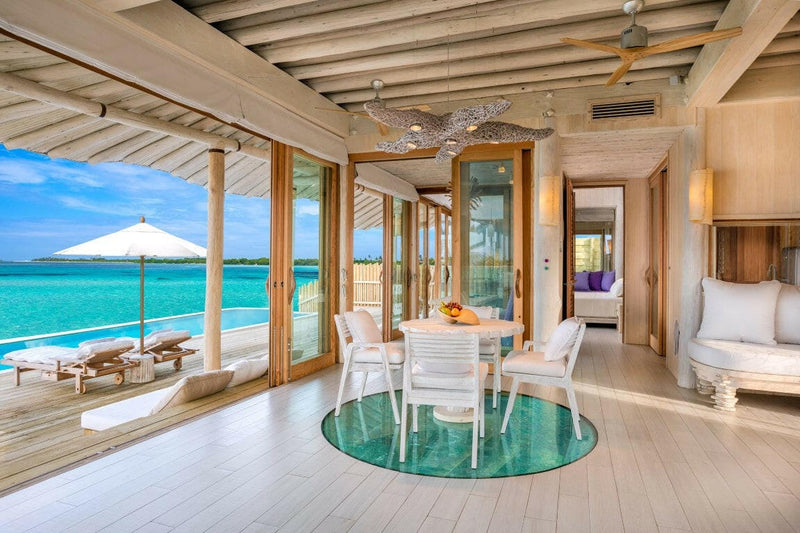 A villa interior at Soneva Jani, a white dining table on a round rug with the deck parasol beyond.