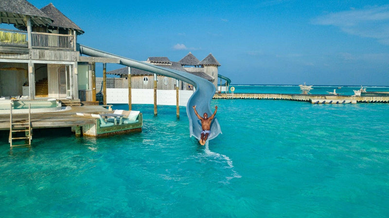 A guest riding the water slide at Soneva Jani, dropping from the villa deck into the turquoise lagoon.