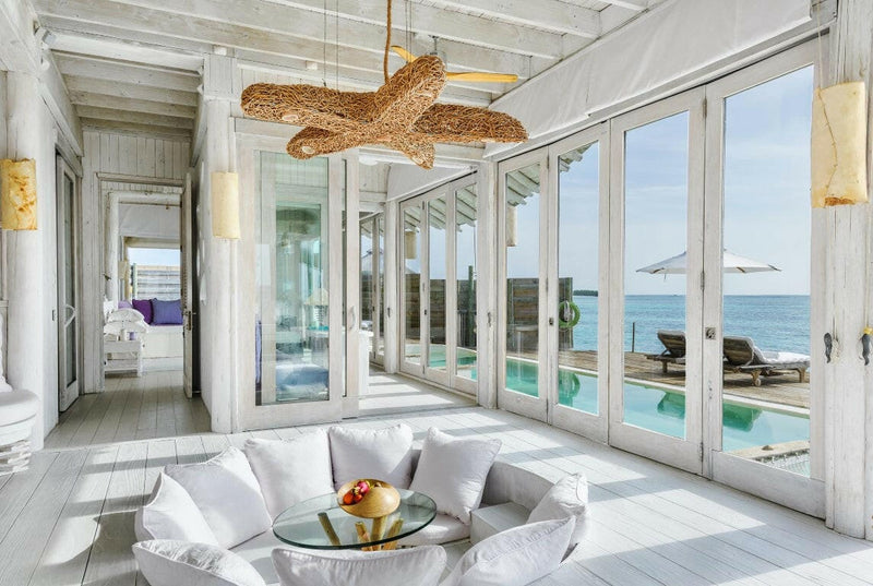 A villa living room at Soneva Jani, a round white sofa under a woven starfish light between glass doors.