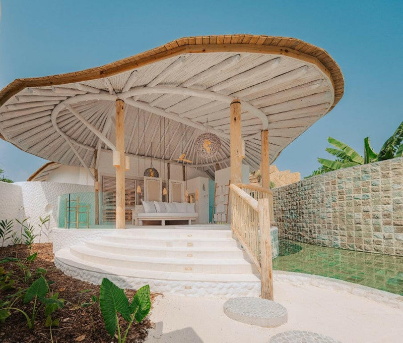 An outdoor bathroom at Soneva Jani, a woven fan canopy above green mosaic tiles and tropical planting.