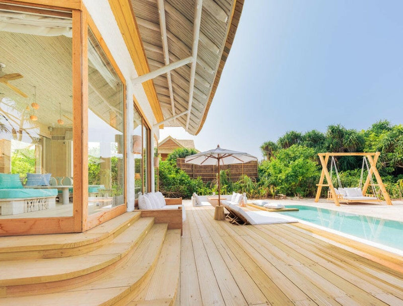 A villa deck at Soneva Jani, curving pale boards past a lounger and swing seat to the private pool.