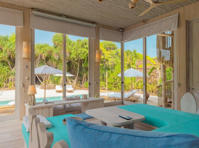A villa living area at Soneva Jani, a low white sofa with the pool and loungers through the glass.