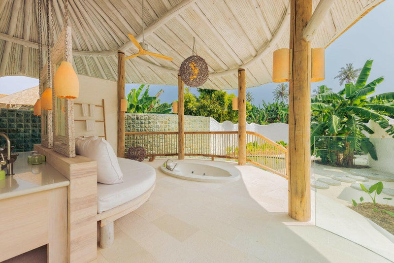 A villa bathroom at Soneva Jani, a round sunken tub under hanging lanterns beside a green mosaic wall.