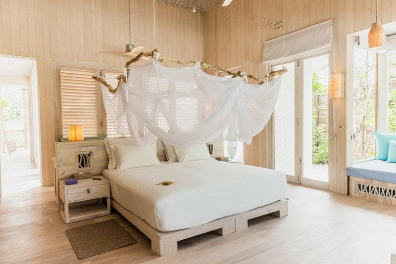 A villa bedroom at Soneva Jani, a white four poster draped in netting on a pale timber floor.