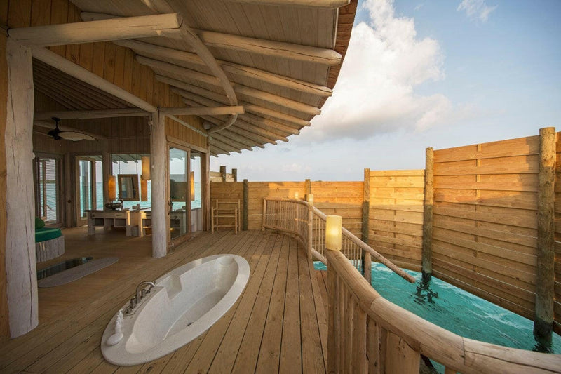 A villa deck at Soneva Jani, a round bath sunk into the timber floor behind a curved privacy screen.
