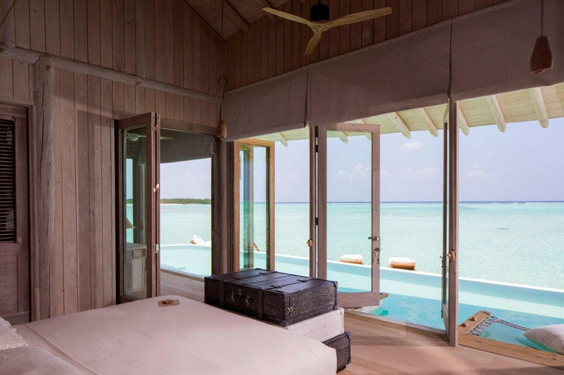 A villa interior at Soneva Jani, pale timber walls and a dark trunk with doors folded back to the lagoon.