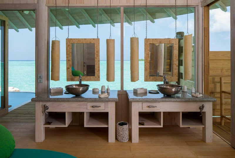 A villa bathroom at Soneva Jani, carved wooden bowls as basins on twin timber vanities open to the green.