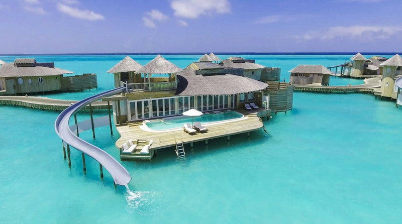 A water villa at Soneva Jani from the air, a white slide curling from the upper deck into the lagoon.