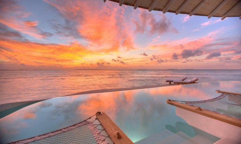 Sunset at Soneva Jani, pink cloud over a pool running to the sea with a hammock net in the foreground.