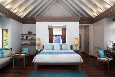 A Beach Villa bedroom at Anantara Dhigu, bed and bench on a blue rug under a pitched white ceiling