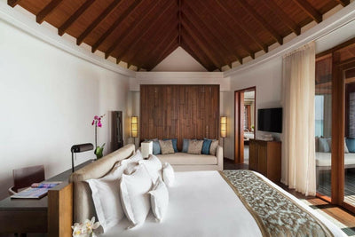 An Over Water Suite bedroom at Anantara Dhigu under a timber ceiling, with a patterned bed runner
