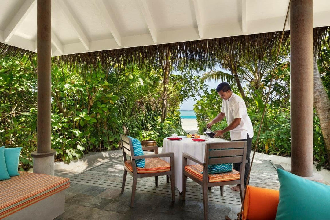 A waiter laying breakfast on the terrace of a Sunrise Beach Villa at Anantara Dhigu, the sea beyond