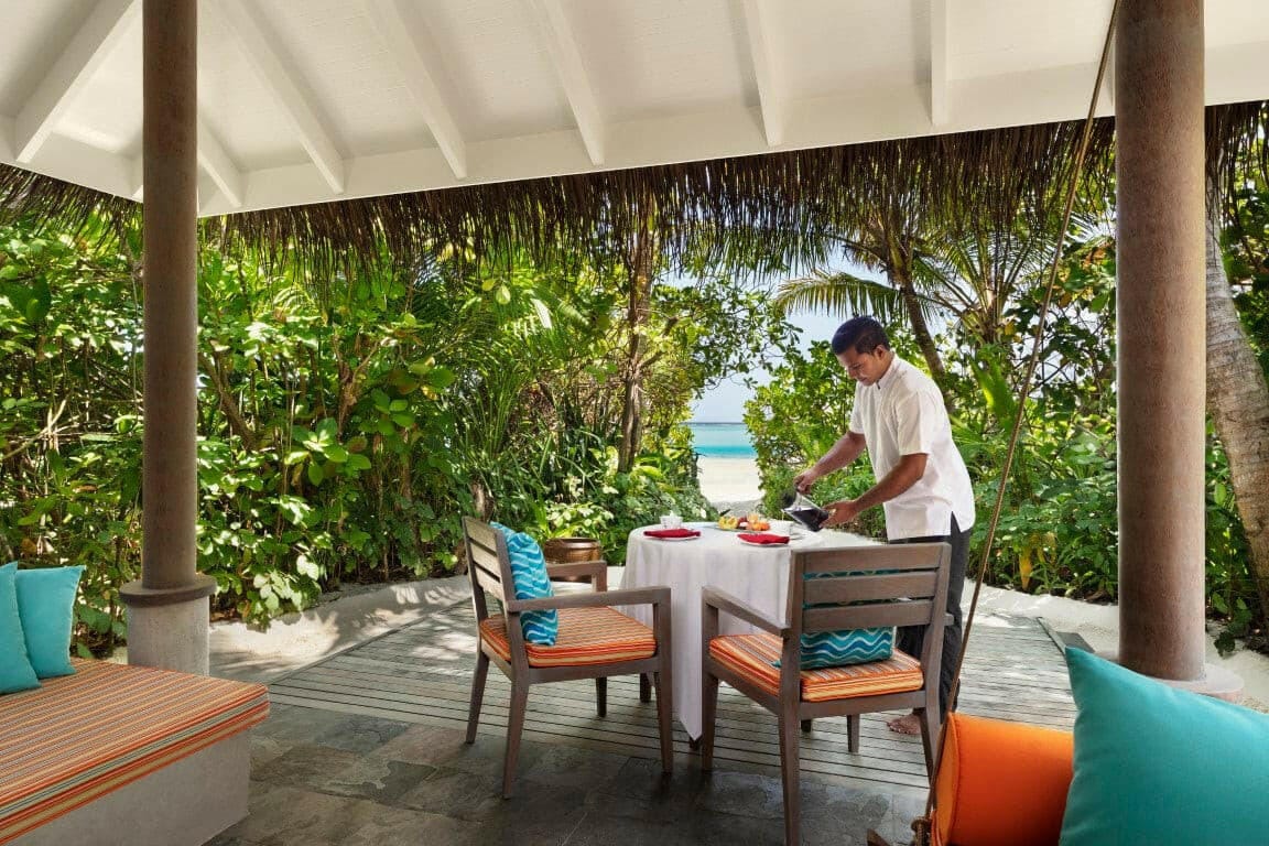 A waiter laying breakfast on the terrace of a Sunrise Beach Villa at Anantara Dhigu, the sea beyond