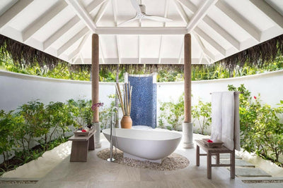 The walled garden bathroom of a Sunset Beach Villa at Anantara Dhigu, freestanding bath on a bed of pebbles