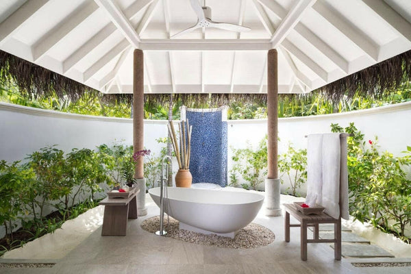 The walled garden bathroom of a Sunset Beach Villa at Anantara Dhigu, freestanding bath on a bed of pebbles