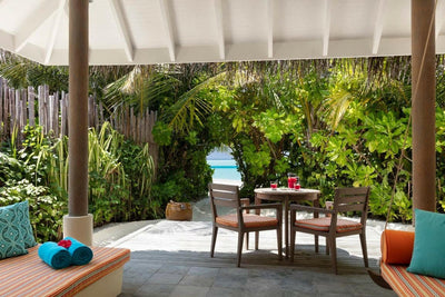 The terrace of a Sunset Beach Villa at Anantara Dhigu, table and cushioned bench beside the greenery