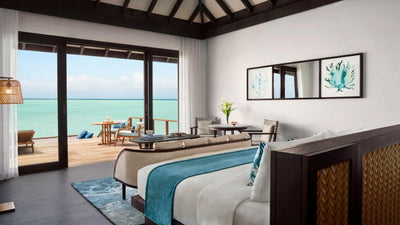 A Deluxe Over Water Pool Villa bedroom at Anantara Veli, coral artwork above the bed and doors to the deck