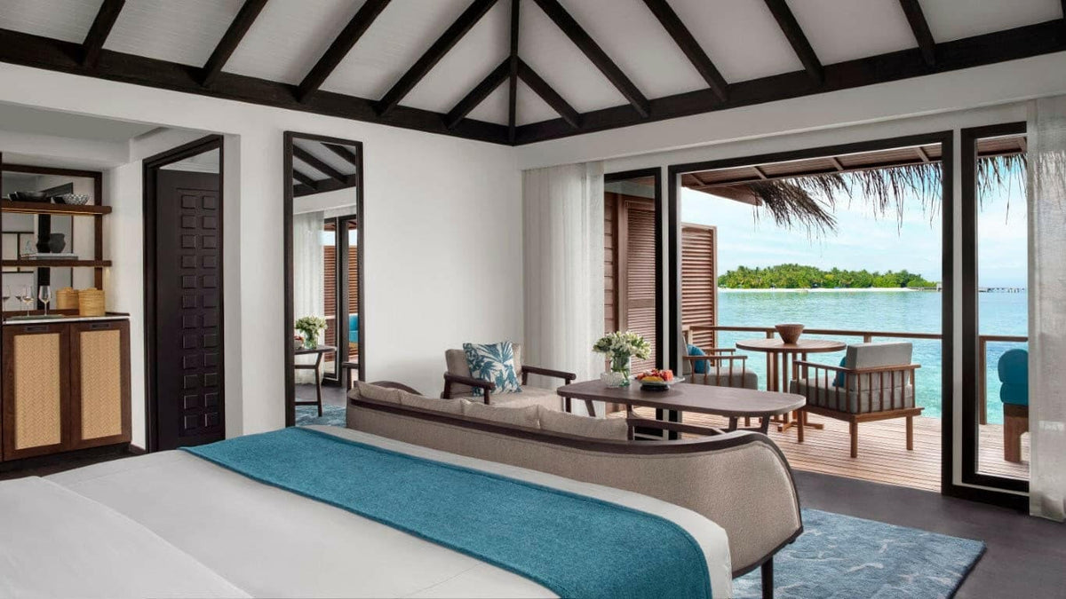 A Superior Over Water Villa bedroom at Anantara Veli, doors open to the deck and the lagoon