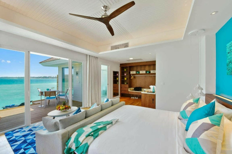 An overwater villa at Kandima Maldives, turquoise cushions and a blue patterned rug by the deck doors.