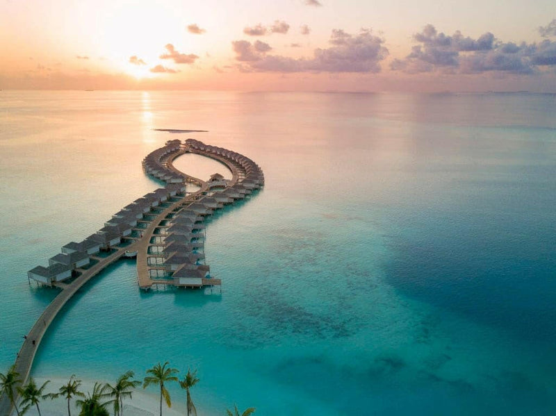 Kandima Maldives at sunrise, a curving jetty of overwater villas reaching into the sea.