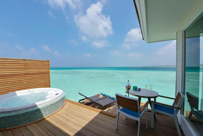 The deck of an overwater villa at Kandima Maldives, a round tub and a table set over the lagoon.