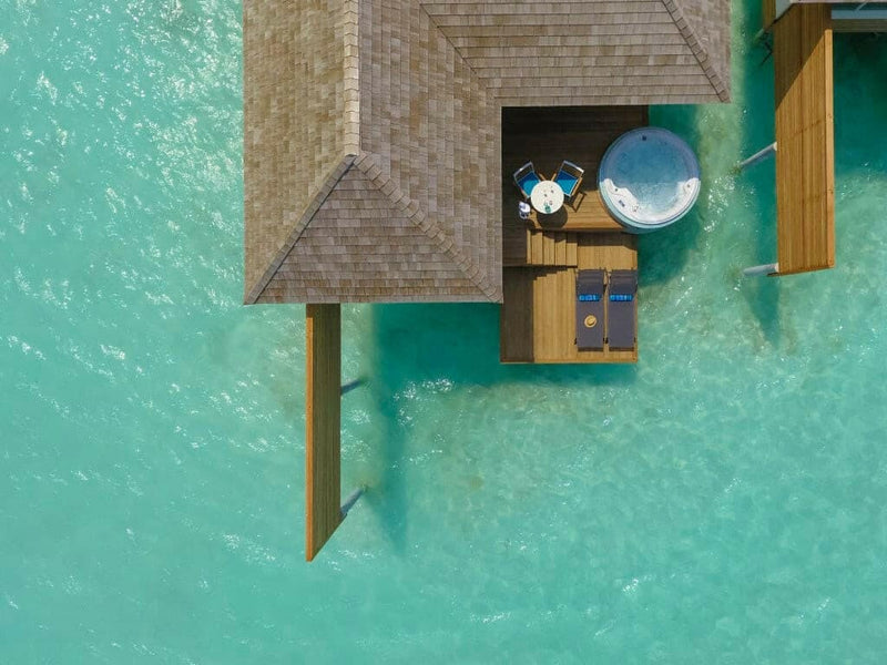 Looking down on an overwater villa at Kandima Maldives, its shingle roof and round deck tub.