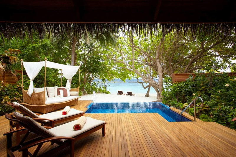 A villa pool at Baros Maldives, a curtained daybed and fruit tray on the deck under dense greenery.