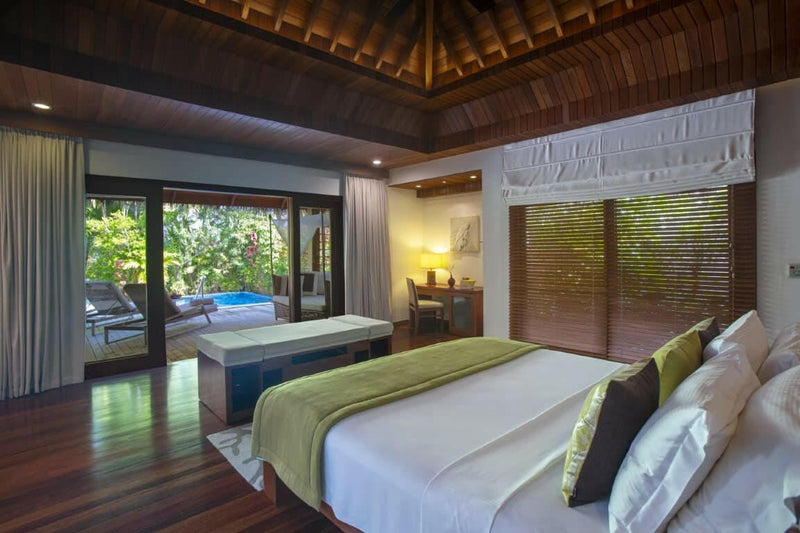 A villa bedroom at Baros Maldives, louvred timber shutters and doors opening onto the pool terrace.