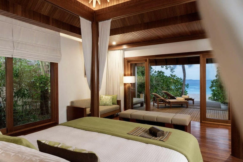 A villa bedroom at Baros Maldives, an olive runner on the bed with loungers on the terrace beyond.