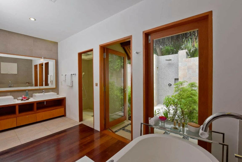 A villa bathroom at Baros Maldives, a timber vanity beside a planted outdoor shower court.
