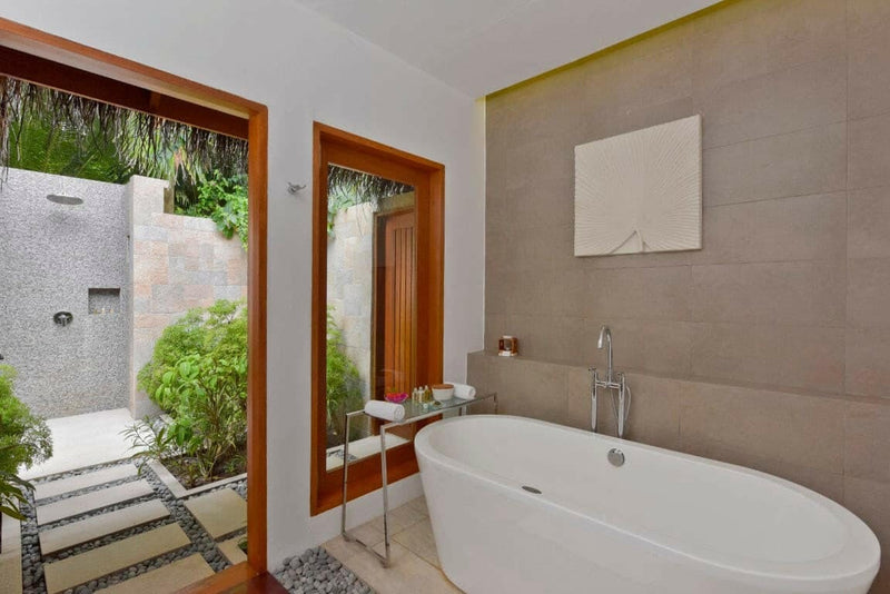 A villa bathroom at Baros Maldives, a freestanding tub facing stepping stones into an outdoor shower.
