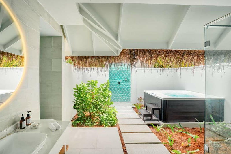 An open-air bathroom at Nova Maldives, a black jacuzzi tub set in planting beside a green tiled wall.