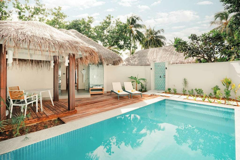 A walled garden pool at Nova Maldives, turquoise water, timber deck and a thatched villa behind.