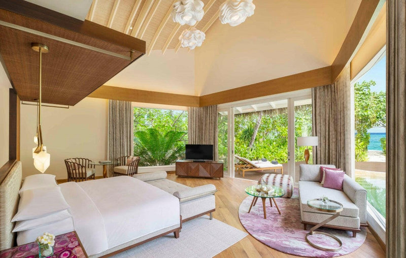 A beach villa bedroom at JW Marriott Maldives, magenta rug and cushions with garden through the doors.