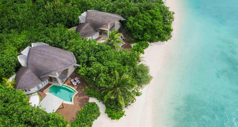 Beach villas at JW Marriott Maldives from the air, thatched roofs in thick greenery above white sand.