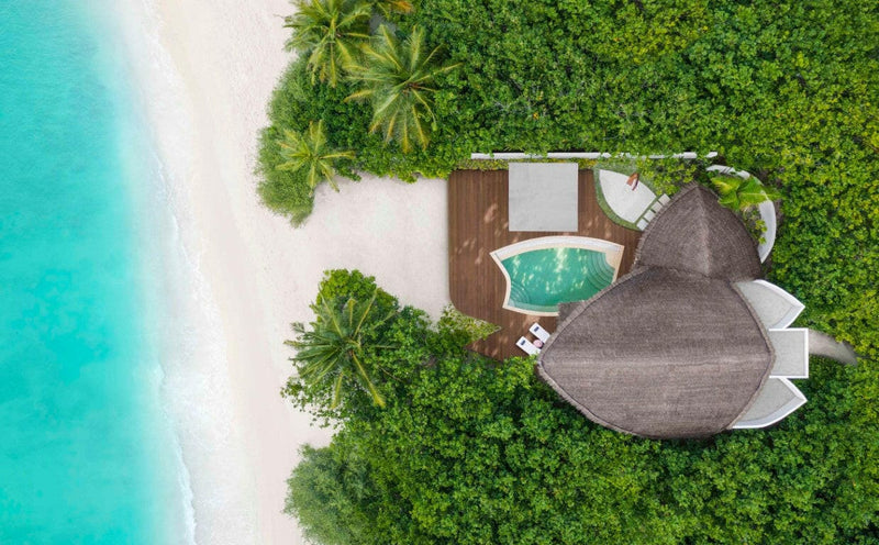 A beach villa at JW Marriott Maldives from above, green plunge pool set among palms beside the sand.